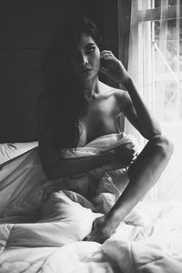 Portrait of shirtless woman sitting on bed at home