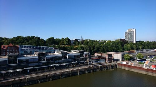 Bridge over river by buildings against clear blue sky