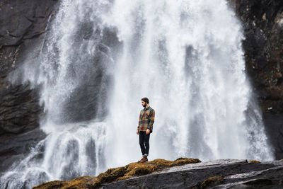 Male hiker standing on hill near waterfall in highland area in winter