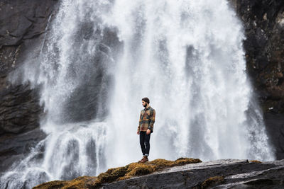 Man standing on rock against waterfall