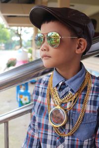 Close-up of boy wearing sunglasses and gold chains by railing