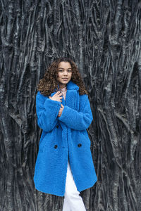 Portrait of a smiling young woman standing against tree trunk