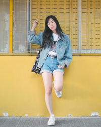 Portrait of young woman leaning on yellow wall