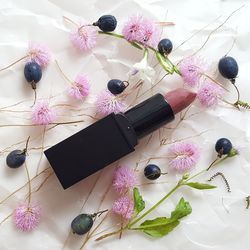 Directly above shot of lipstick surrounded with berries and flowers on table