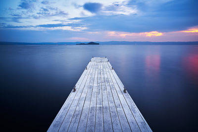 A wooden pier on bolsena lake at sunrise with isola bisentina on the background and a long exposure