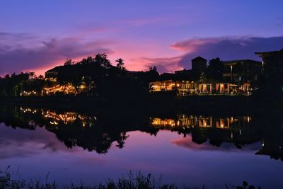 Silhouette buildings by lake against sky during sunset