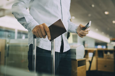 Midsection of businessman holding passport and smart phone at airport