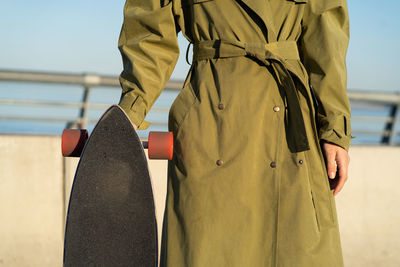 Closeup of casual girl with longboard standing over blue sky. hipster stylish woman hold skateboard