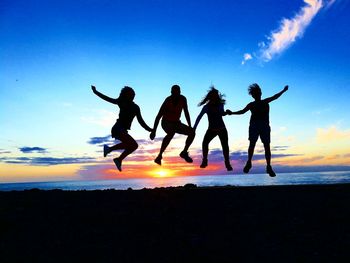 Full length of silhouette friends jumping at beach during sunset