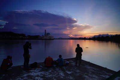 Silhouette people on footpath by lake against sky during sunset