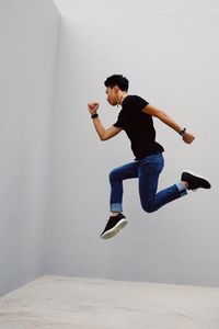 Side view of man jumping against white wall