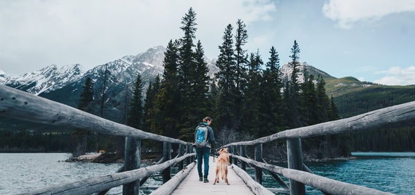 Woman standing on footbridge by lake against sky