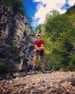 Portrait of young woman with bicycle on rock against sky