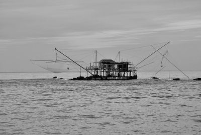 Fishing hut on stilts in sea against sky