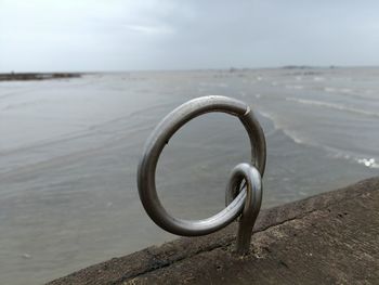 Close-up of metal chain on beach against sky