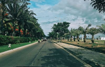 Treelined road against cloudy sky