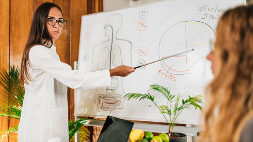 Female nutritionist standing in front of the white board smiling and explaining meal plan 