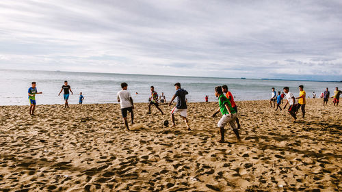 People playing soccer at beach against sky