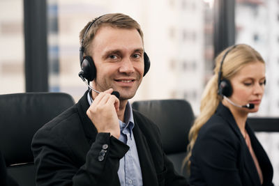 Portrait of smiling man wearing headset by colleague in call center