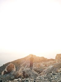 Rear view of man standing on rock against sky