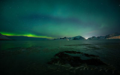 Scenic view of sea by snowcapped mountains against sky at night