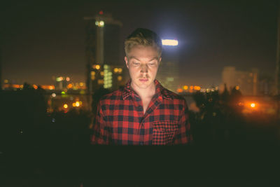 Portrait of young man looking at illuminated city at night