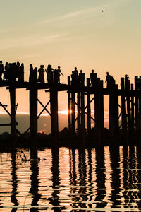 Silhouette people standing on pier over sea against sky during sunset