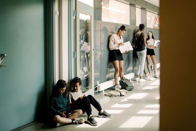 Boy and girl sitting in doorway while junior high students talking in school corridor
