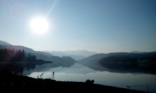 Silhouette of trees amidst lake against sunshine