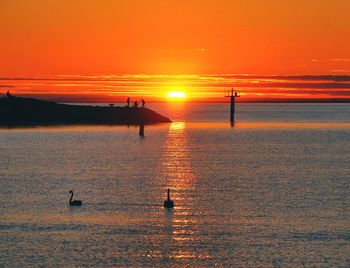 Silhouette people on sea against orange sky during sunset