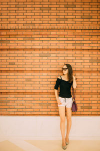 Full length of young woman standing against brick wall