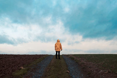 Woman standing on road against cloudy sky