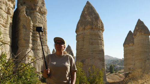 A woman films herself on an action camera against a backdrop of sandstone cliffs.  girl is blogging