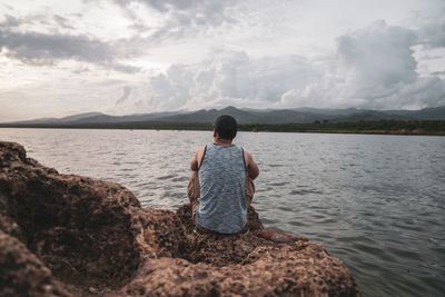 Rear view of man looking at lake against sky