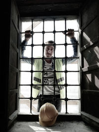 Portrait of young man standing against window in building