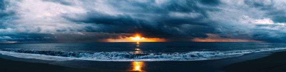 Panoramic view of beach against cloudy sky at sunset