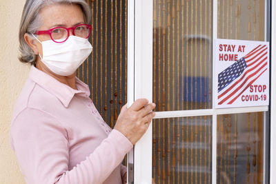 Portrait of senior woman wearing mask standing at house entrance