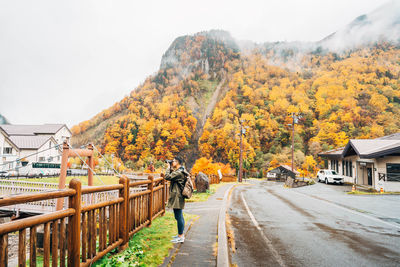 Road amidst trees and houses against sky during autumn