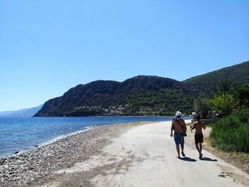 Rear view of men walking on beach against clear blue sky