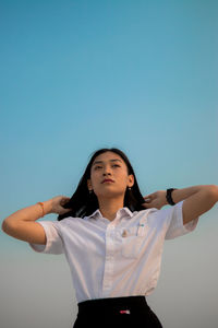 Young woman with hands in hair standing against sky during sunset