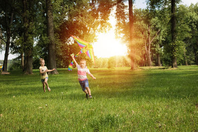 Full length of children running while flying kite on field