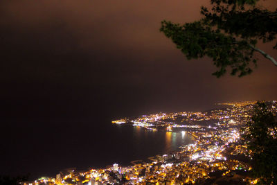 Illuminated city by sea against sky at night