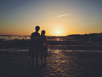 Friends standing at beach against sky during sunset