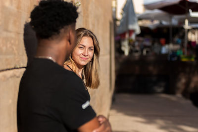 Blonde girl leaning against a wall looking at her black friend.