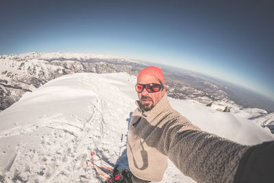 Portrait of man taking selfie while standing on snowy field