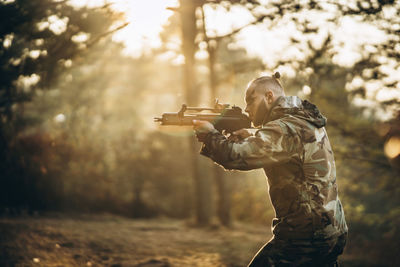 Side view of army soldier aiming gun in forest