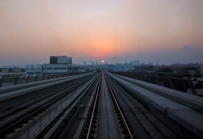 Railroad tracks in city against sky at sunset