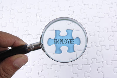 Close-up of hand holding magnifying glass over employee text and jigsaw pieces