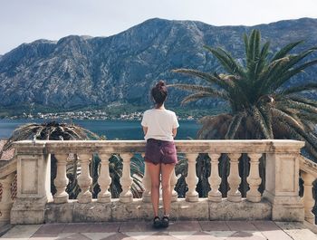 Rear view of woman standing by retaining wall against sky