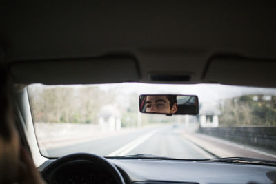 Reflection of man in car rear-view mirror on road